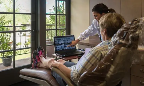 Dr. Lynch pointing to dental X-rays on a laptop while a patient, seen from behind, sits in a treatment chair
